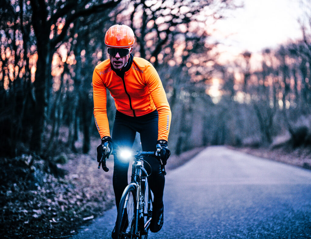 Sports cyclist on a cold day wearing orange bicycle helmet and jacket from FUSION. black googles and pants.